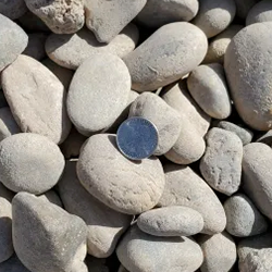 Grey round 1 - 1/2 inch gravel showcased with a quarter for scale. Available at Albuquerque Landscape Supply, this high-quality gravel features a round shape and a beautiful grey color, ideal for creating a natural and timeless look in your outdoor space. Use this gravel to construct walkways, driveways, or as a decorative element to enhance your landscape design.